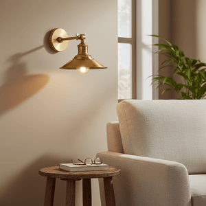 Antique brass wall lamp mounted beside a cozy sofa, illuminating a side table with books and glasses.