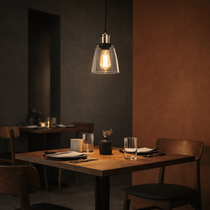 Satin chrome pendant light with clear glass shade illuminating a dining table in a stylish restaurant setting.