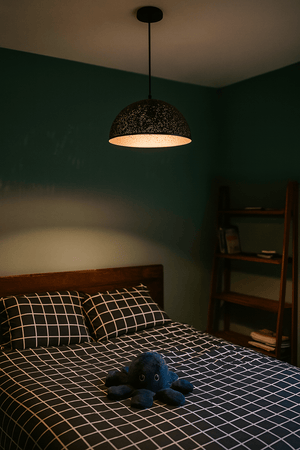 Black metal pendant light with starry cut-out shade hanging above a bed with grid-patterned bedding and a plush toy.