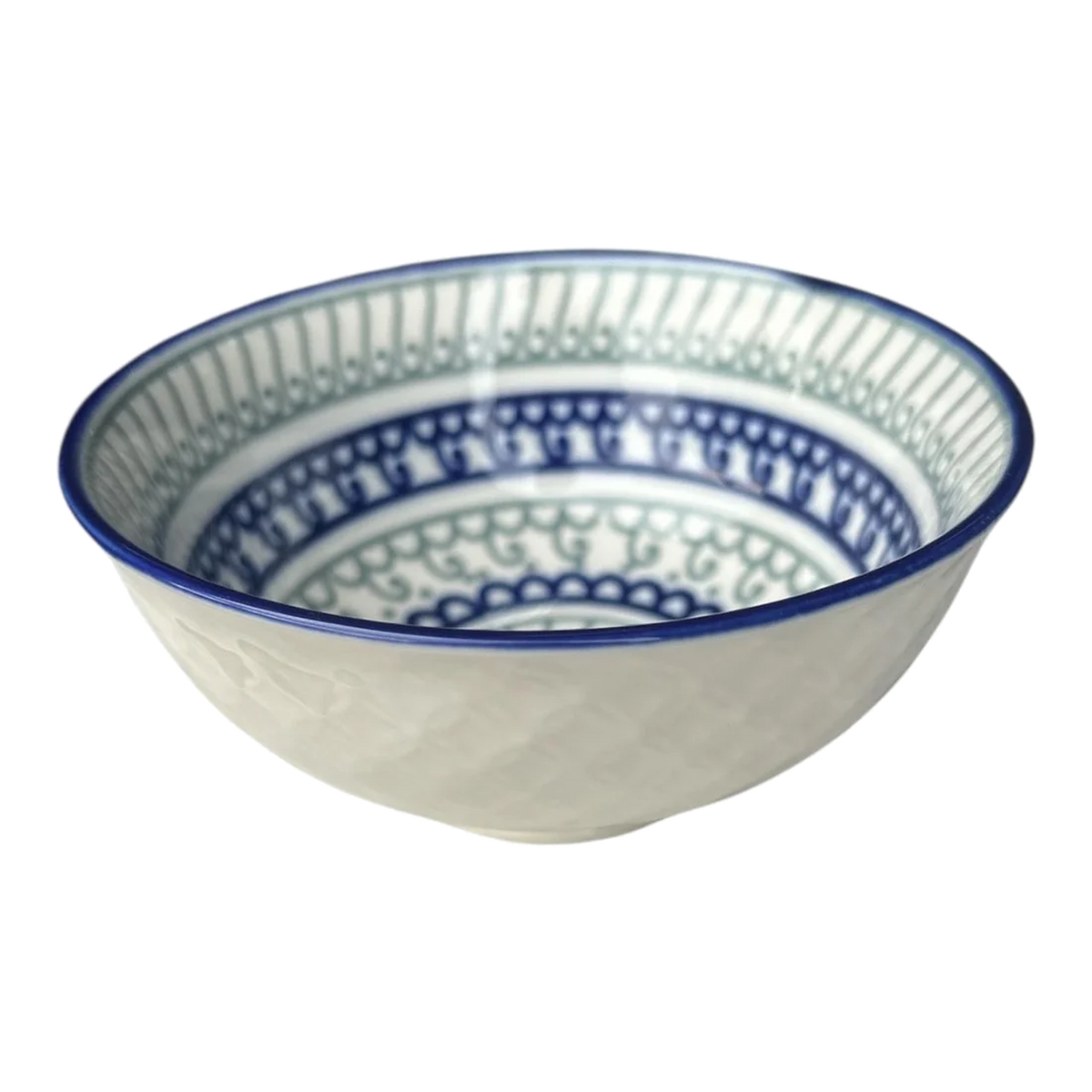 White ceramic bowl with blue rim and blue‑green patterned interior, photographed against a solid green background.
