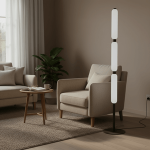 Three‑tier white cylindrical floor lamp on black stand beside a beige armchair in a modern living room.