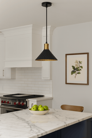 Black iron pendant light with gold accents hanging over a marble kitchen island with green apples.