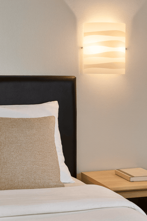 Stylish white patterned glass wall light mounted above a bed, illuminating the space softly.