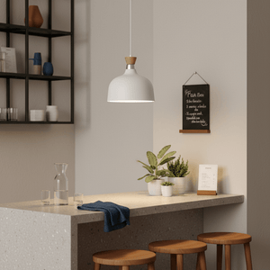 White metal pendant light with wood accent hanging over a kitchen island with plants and glassware.