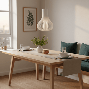 Scandi white pendant light hanging above a wooden dining table set with dishes and greenery.
