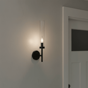 Black metal wall light with clear glass shade mounted on a wall, illuminating a doorway.