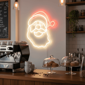 Father Christmas face LED motif light glowing on a cafe wall, above a coffee machine and pastries.