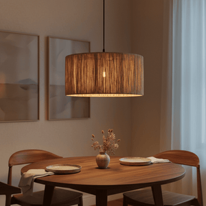 Medium pendant light with woven raffia shade hanging above a wooden dining table set with plates and a vase.