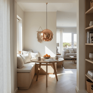 Copper pendant light hanging over a round wooden dining table with a cozy seating nook, bright natural light filling the