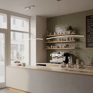 Sleek Maybe Someday Bow LED Pendant light illuminating a modern café counter with pastries and coffee machine.