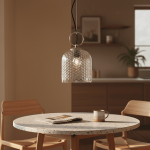 Clear glass pendant light hanging above a round table with a coffee cup and magazine.