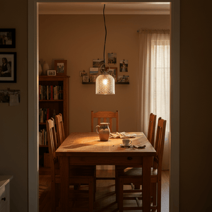 A clear glass pendant light hangs above a wooden dining table set for a meal, with warm lighting.