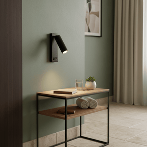 Cosima bedside reading light mounted on a green wall, illuminating a wooden table with a glass and plant.