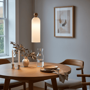 Fluted white-glass pendant light with gold trim hanging above a wooden dining table set with decor.