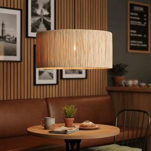 Clocolan Raffia Large Pendant Light hanging above a wooden table with a coffee cup, plant, and pastry.