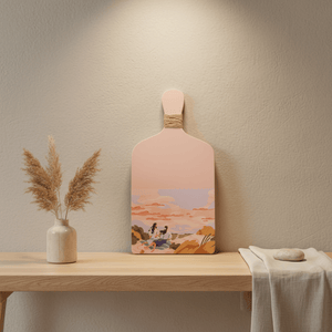 Light pink decorative kitchen board with a scenic illustration, placed on a wooden shelf with dried flowers.