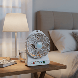 Rechargeable portable mini fan on a bedside table next to a lamp and glasses, providing airflow.