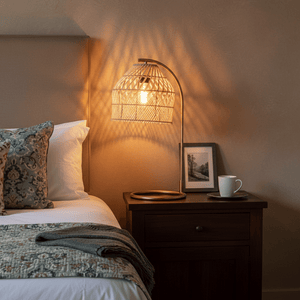 Coghlan Rattan Table Lamp illuminating a bedside table with a cozy setup, featuring a woven shade and warm light.