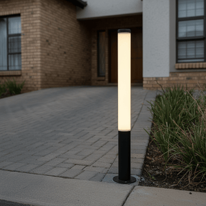 20W black LED bollard light illuminating a driveway, surrounded by grass and brick house facade.