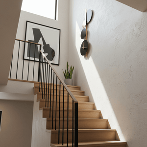 Stylish black and gold wall light with clock mounted on a stairwell wall, complemented by a modern art piece.