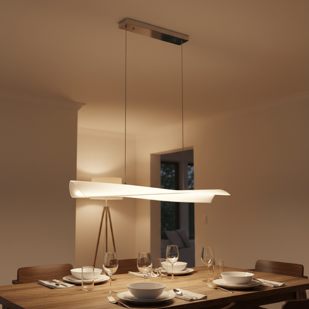 Polished chrome and acrylic pendant light hanging over a dining table set with plates and glasses.