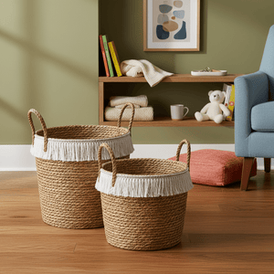 Two woven storage baskets with white fringe on a wooden floor, surrounded by a cozy living space.