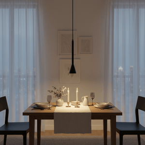 A sleek black pendant light hangs over a wooden dining table set with plates, glasses, and candles, creating a cozy ambiance.