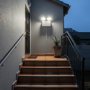 Emergency twin LED floodlight mounted on a wall illuminating outdoor stairs at dusk.