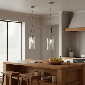 Two clear glass pendant lights hang above a wooden kitchen island with a bowl of fruit.