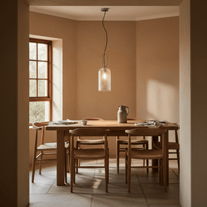 A clear glass pendant light hangs above a wooden dining table set with plates and a pitcher in a warm-toned room.