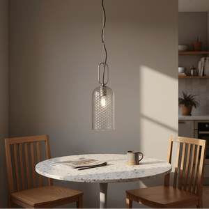 Clear glass pendant light hanging above a round table with wooden chairs, illuminated softly.