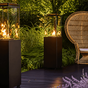 Two Fire Cube space heaters with flames, surrounded by greenery and a wicker chair on a wooden deck.