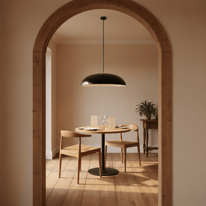 Black oval pendant light hanging above a round dining table with wooden chairs and a plant in a cozy setting.