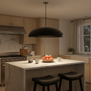 Black oval pendant light suspended above a kitchen island with a bowl of apples and coffee cups.