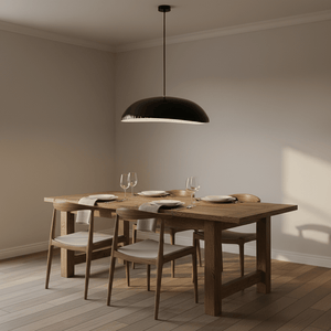 Black oval pendant light suspended above a wooden dining table set with plates and glasses.