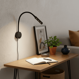 Flexible rubber arm LED reading light mounted on a wall above a wooden desk with a notebook and plants.