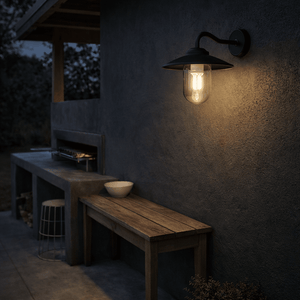 Black metal and glass outdoor wall light illuminating a patio area with wooden furniture.