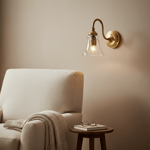 Antique brass wall lamp with clear glass diffuser above a cozy armchair and side table.