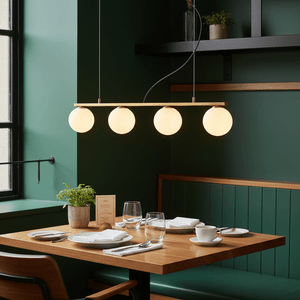 Linear 4 Light Pendant in gold above a dining table with white plates and glasses, set against a green wall.