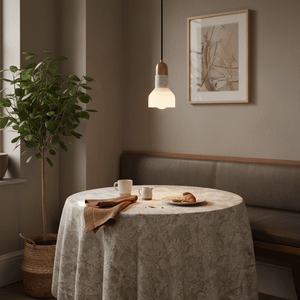 A stylish pendant light hangs over a dining table set with cups and a plate of croissants, surrounded by greenery.