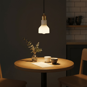 A stylish pendant light with a white marble shade and gold trim hanging above a wooden table with two cups and a vase.