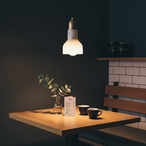 A stylish pendant light with a white marble shade and gold trim hanging over a wooden table with coffee cups and a vase.
