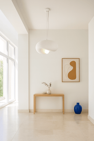 Ivory Drift 300 Pendant Light hanging above a wooden console table with decorative items and artwork.
