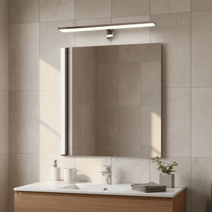 Polished aluminium mirror light mounted above a bathroom mirror, illuminating a sleek vanity with neutral tiles.