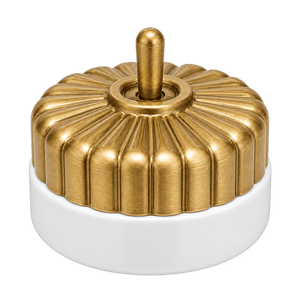 Brushed brass switch with a fluted design atop a white porcelain base, featuring a central toggle.