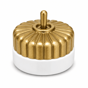 Brass switch with a fluted design atop a white porcelain base, featuring a central toggle.