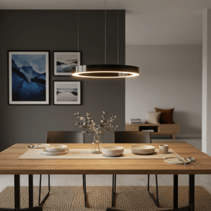 A small black LED halo pendant light hangs above a wooden dining table set with plates and a vase.