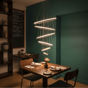 Gold Mega Ribbon LED pendant light hanging above a wooden dining table set with plates and cutlery.
