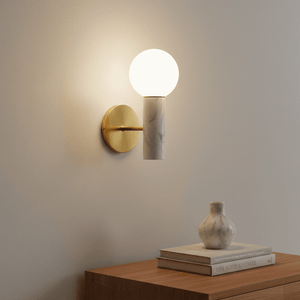 Ollie White Marble Wall Light mounted on a wall, featuring a round glass bulb and antique brass details, with a vase and