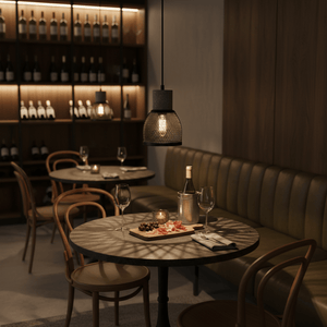 Stylish pendant light casting shadows over a dining table with wine and charcuterie in a cozy restaurant setting.